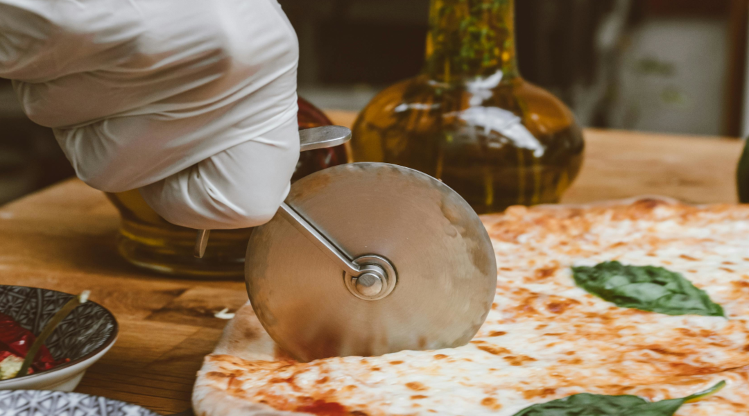 A hand using a pizza slicer on a pizza