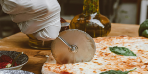 A hand using a pizza slicer on a pizza